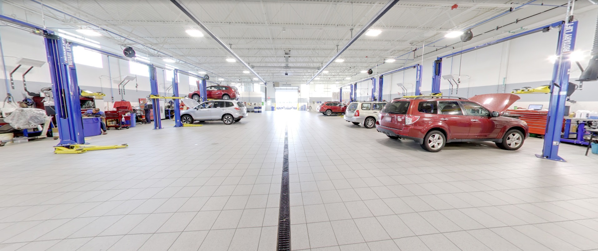 Wide interior view of a bright, modern auto repair garage with multiple vehicle lifts and cars in service.