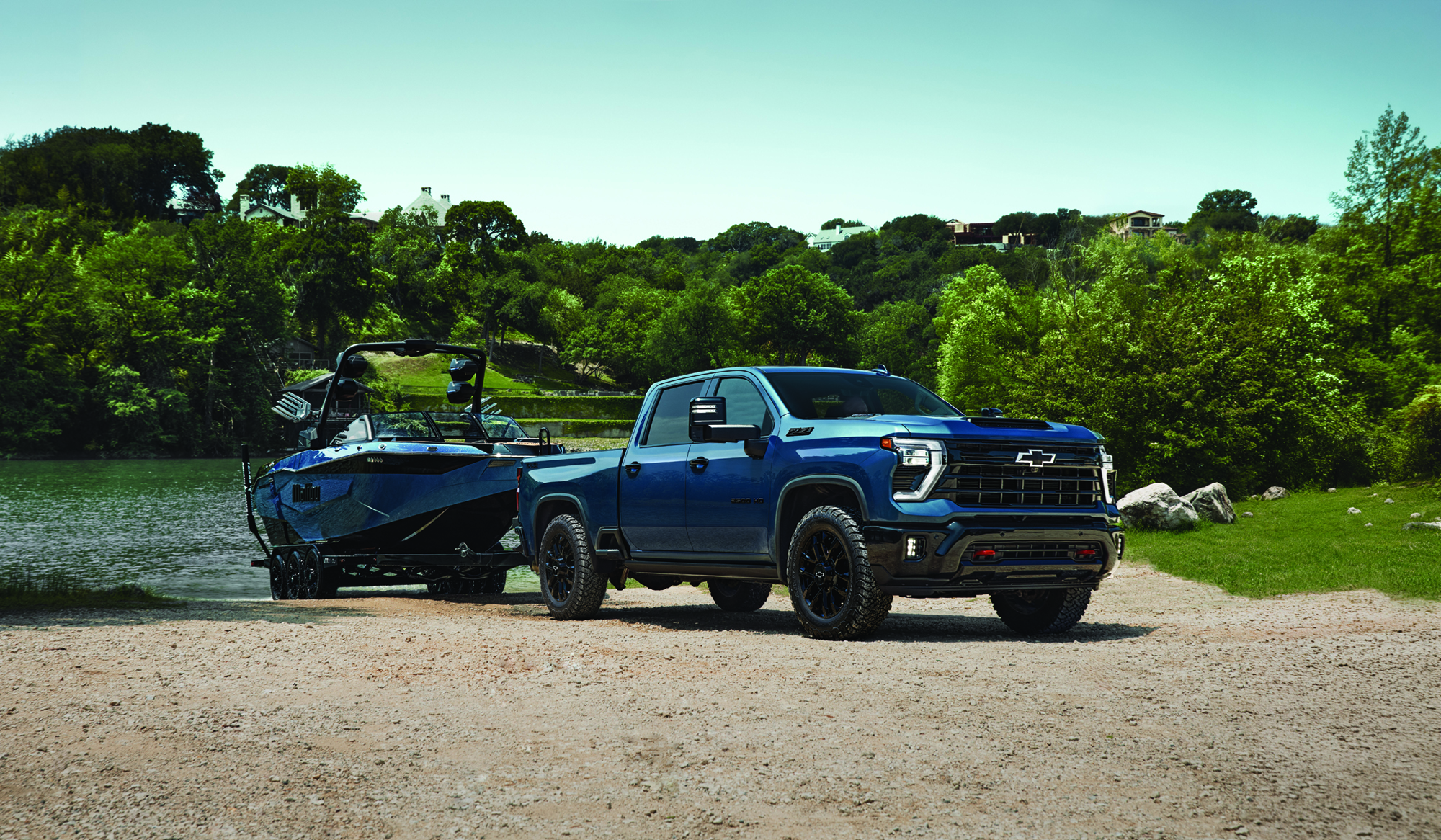 Blue Chevrolet Silverado HD pickup truck towing a matching blue Malibu boat at a lakeside boat launch.