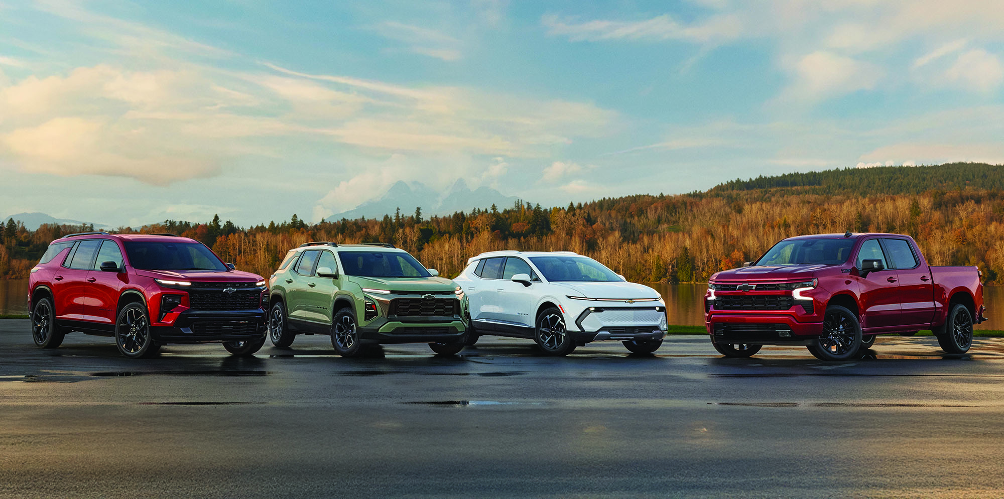 Four Chevrolet SUVs and a pickup truck parked side by side in a scenic outdoor landscape near a lake.