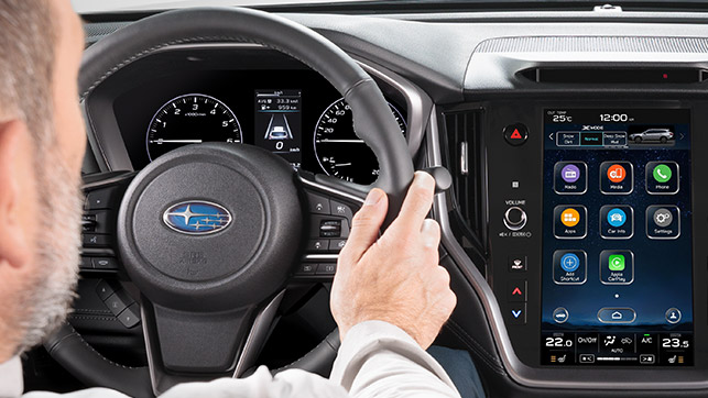 Interior view of a Subaru dashboard, showing the driver's hands and the infotainment screen.