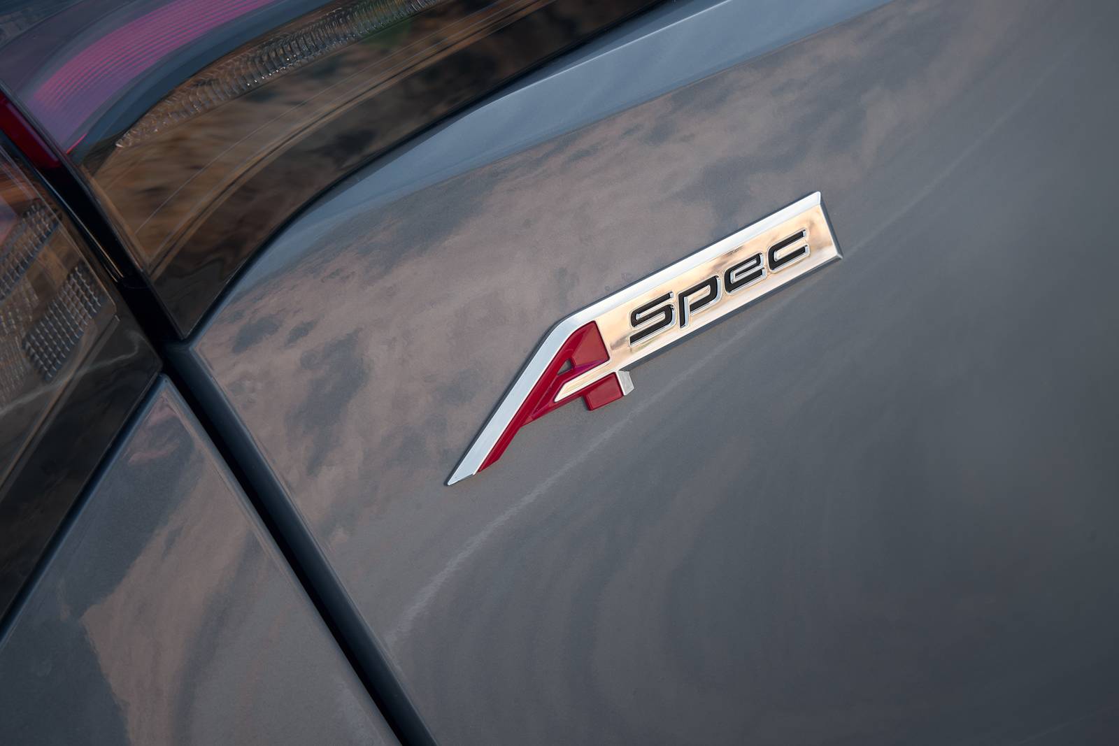 Close-up of an Acura A-Spec chrome and red emblem on a grey car body.
