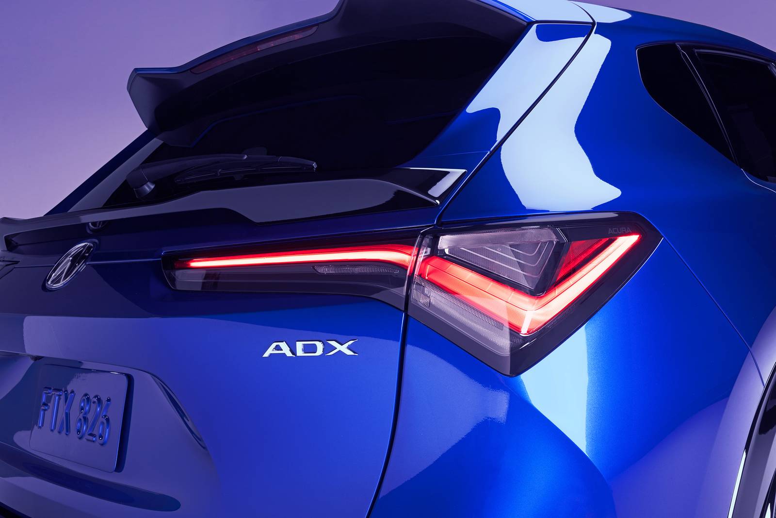 Close-up rear view of a blue Acura ADX with illuminated chicane-style LED taillights and rear spoiler.