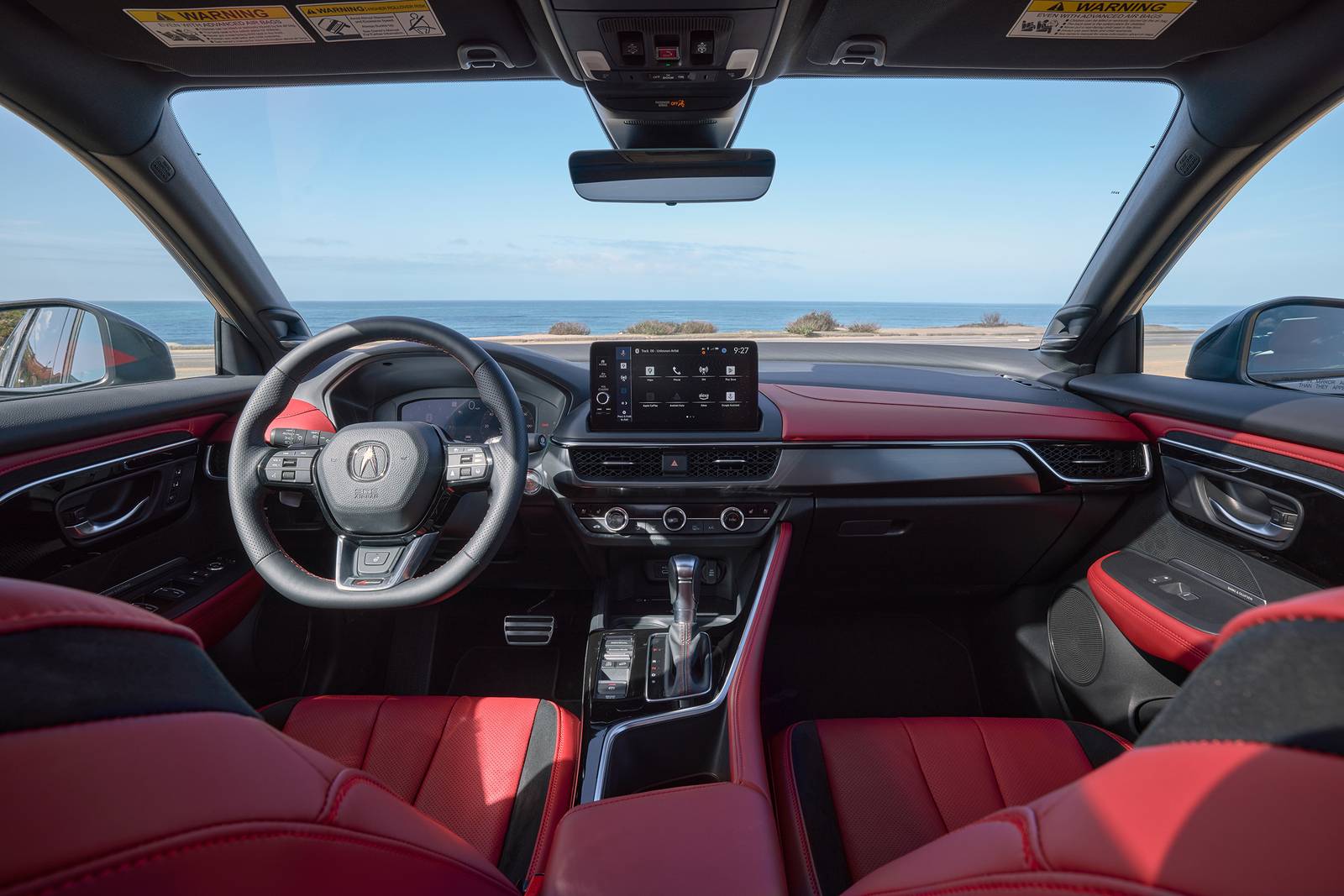 Interior view of an Acura Integra with red and black leather seats, showing the dashboard and a coastal view.