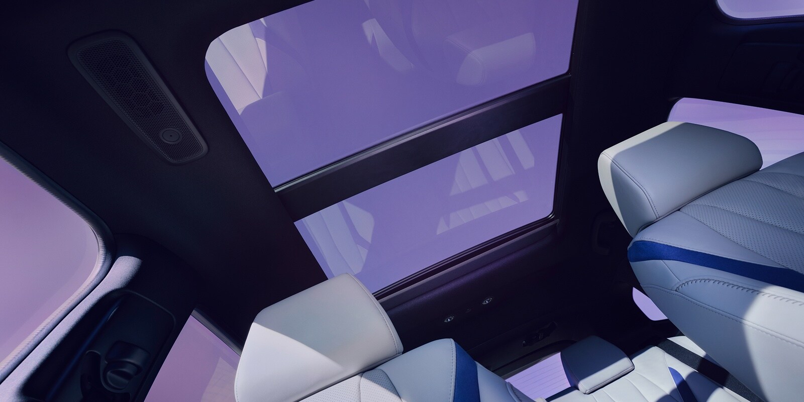Interior view of a modern car looking up at a dual-pane panoramic sunroof with light purple tinting.