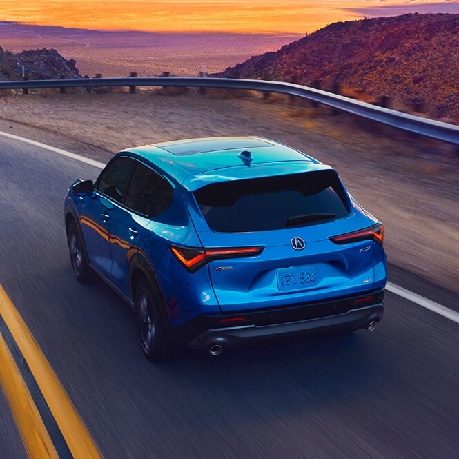 Rear view of a blue Acura ADX driving on a scenic desert road at sunset.