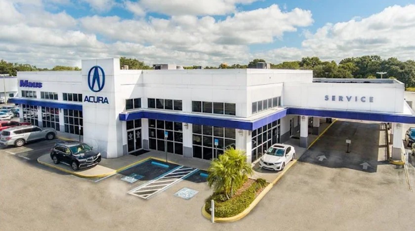 Exterior view of Maus Acura dealership building with service department entrance and parked luxury vehicles.