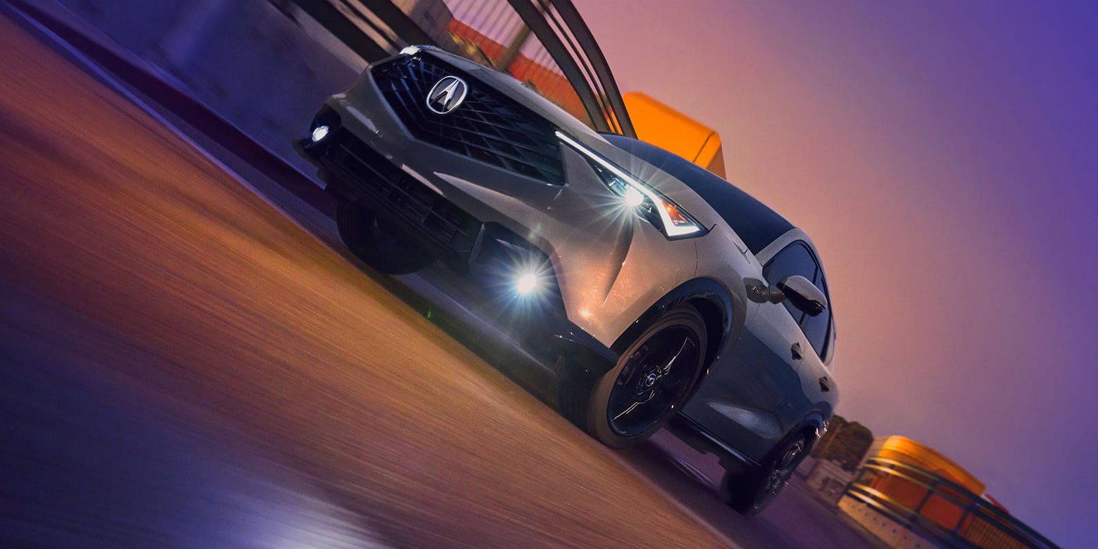 Front view of a silver Acura SUV driving fast along a road under a dramatic purple dusk sky.