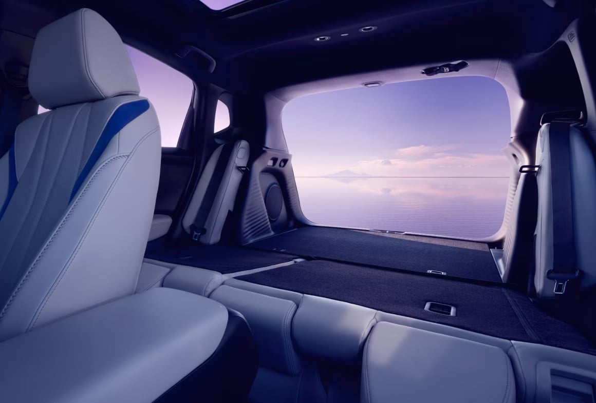Interior of a vehicle with folded rear seats facing a wide open trunk view of a peaceful ocean at twilight.