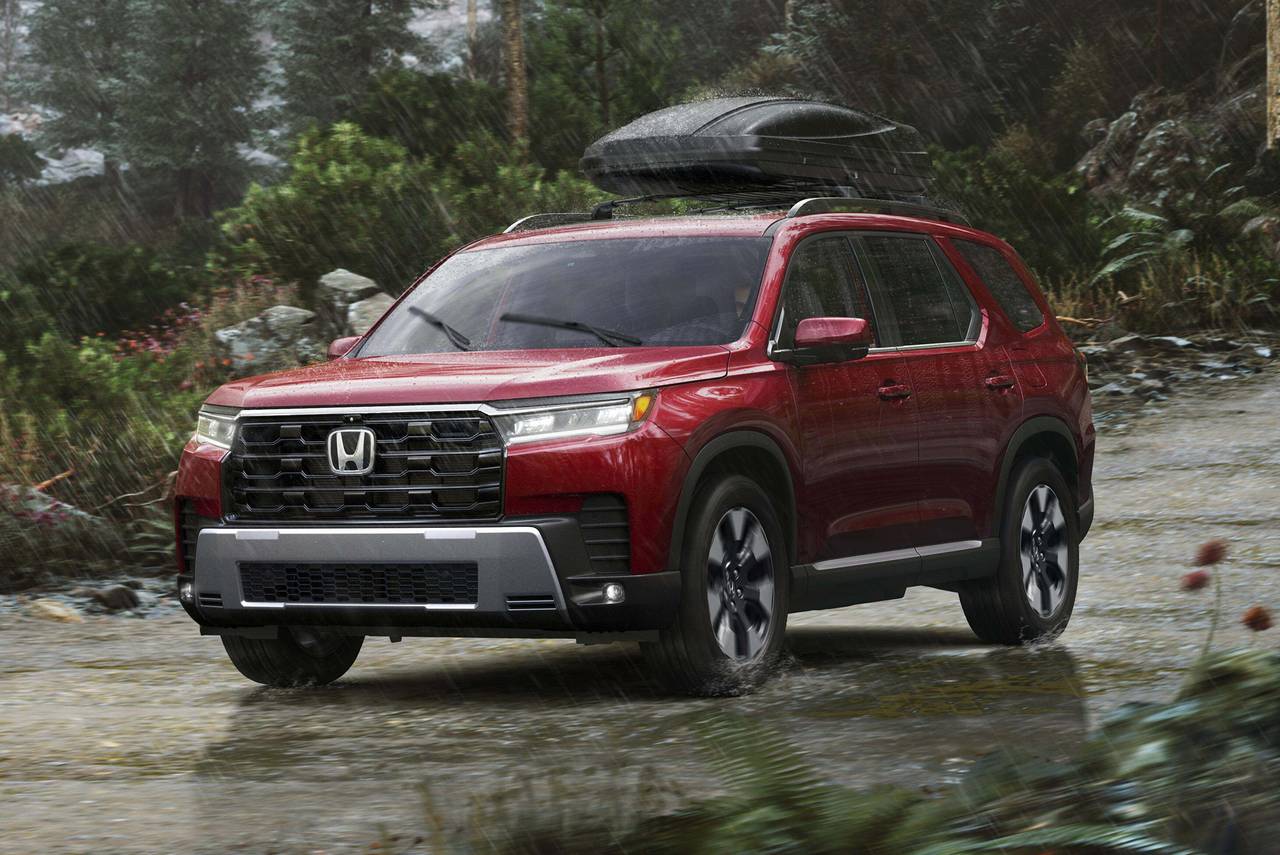 A red Honda Pilot driving through a rainy wooded area with a cargo box on its roof.