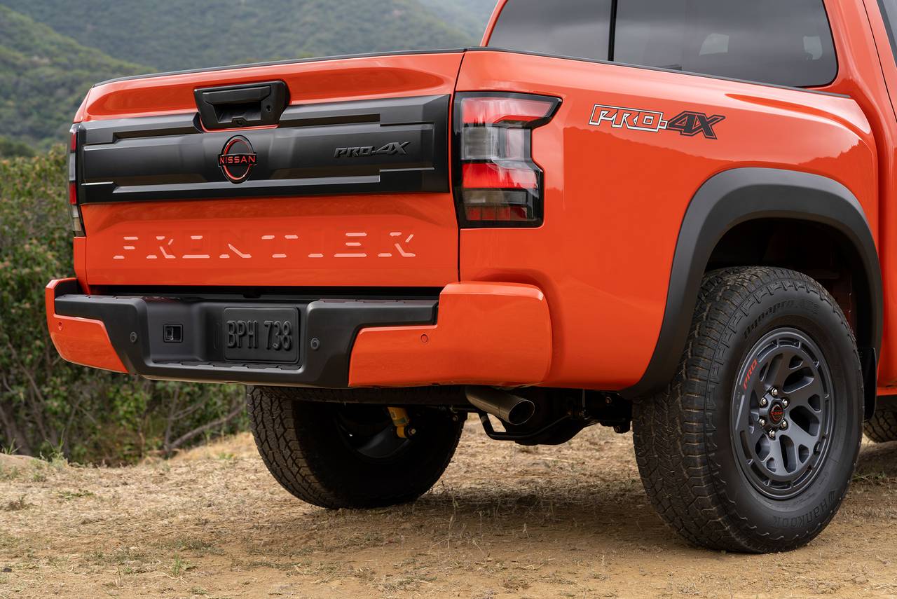 Rear corner view of an orange Nissan Frontier PRO-4X pickup truck on a dirt road.
