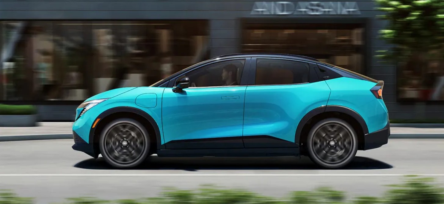 Profile view of a bright cyan Nissan Ariya electric SUV driving along a city street.