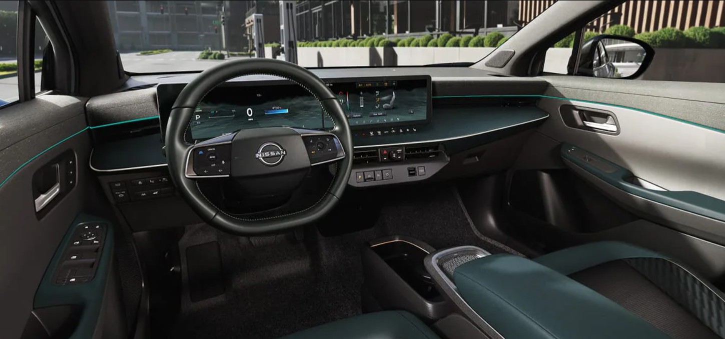 Modern interior of a Nissan Ariya electric vehicle showing the dashboard, dual screens, and steering wheel.