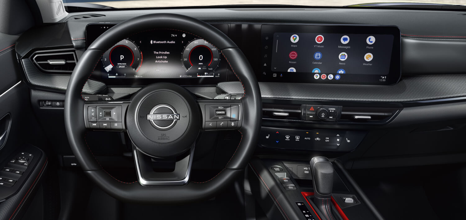 Driver view of a modern Nissan dashboard featuring a leather steering wheel, digital gauge cluster, and touchscreen.