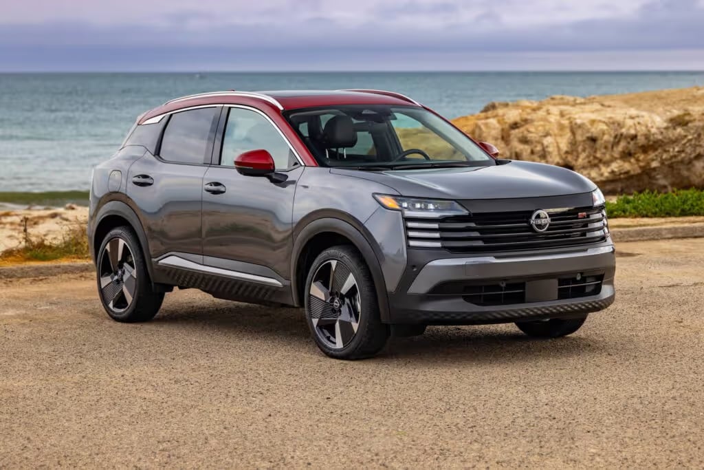 A grey Nissan Kicks SUV with a red roof parked on a coastal lot overlooking the ocean.