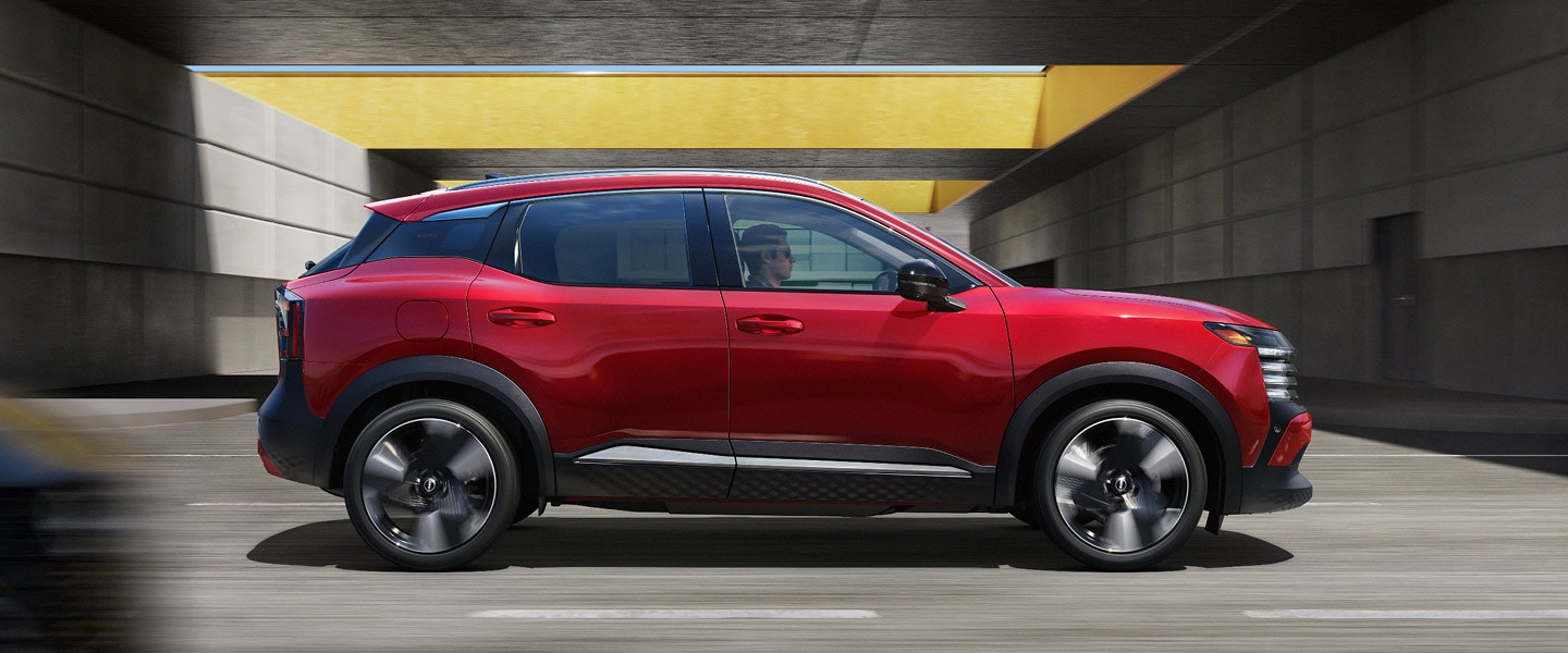 Side profile of a dynamic red compact SUV driving through a modern concrete underpass with a yellow overhead beam.
