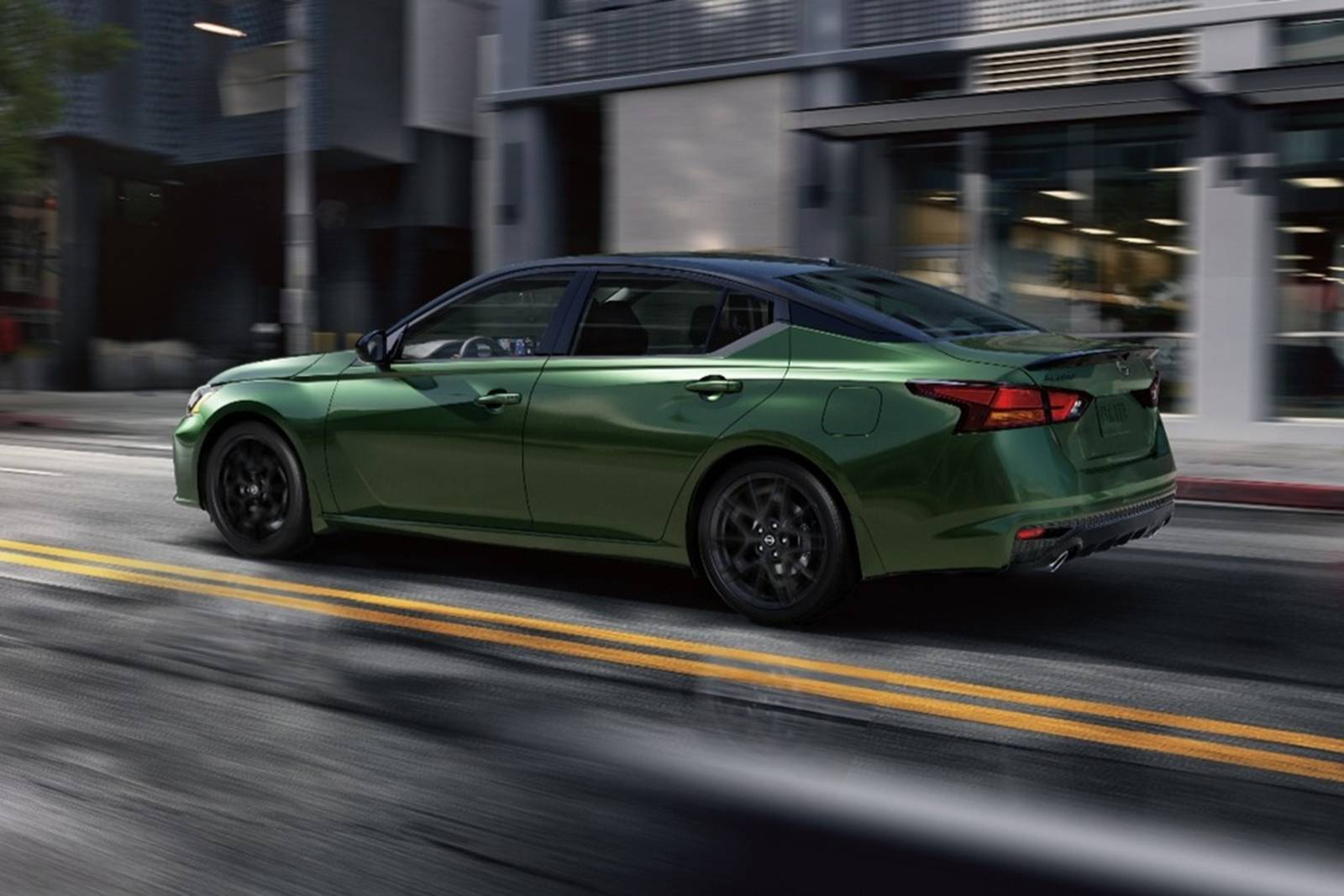 Green Nissan Altima driving down a city street at sunset.