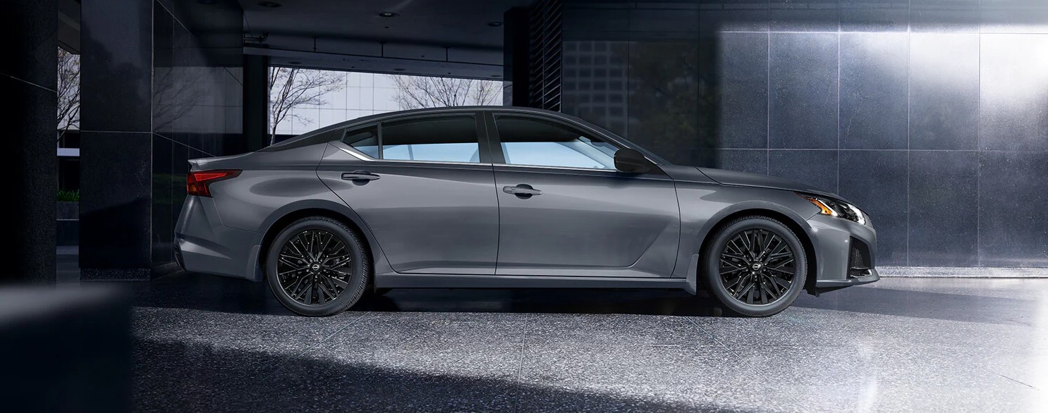 A gray Nissan Altima sedan with black rims parked against a dark, modern building.