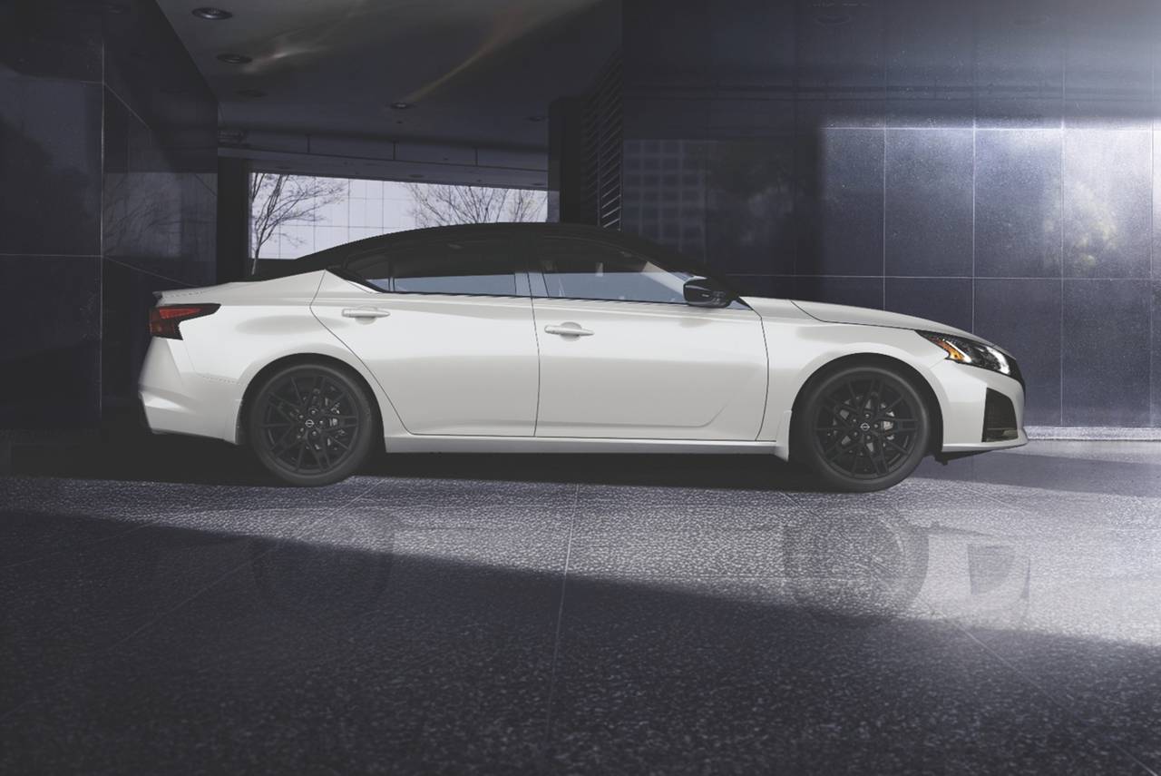 Profile view of a white Nissan Altima with black wheels and a black roof in a modern garage.