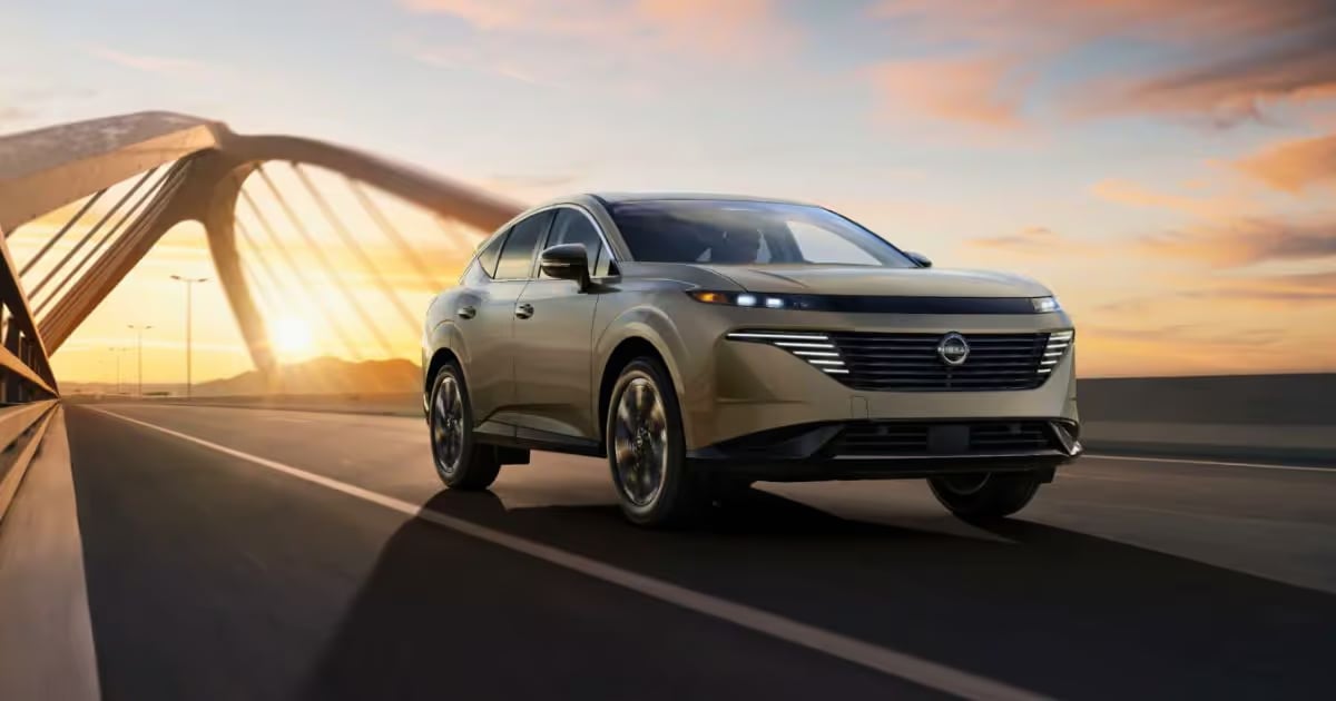 A champagne gold Nissan SUV drives across a modern bridge during a scenic golden hour sunset.