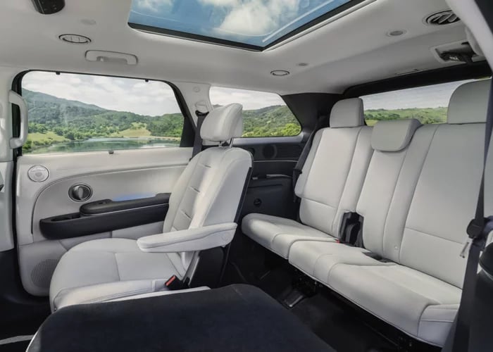 Spacious white leather interior of a three-row SUV featuring a sunroof and scenic window view of green hills.