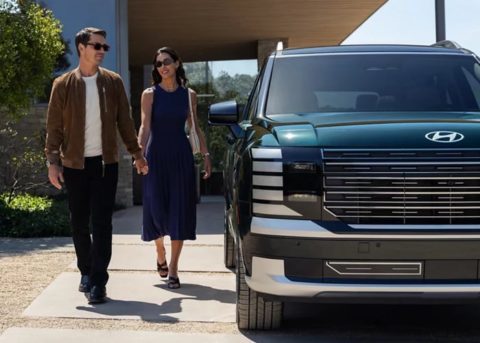 A stylish couple walking hand-in-hand next to a dark green Hyundai SUV on a sunny day.