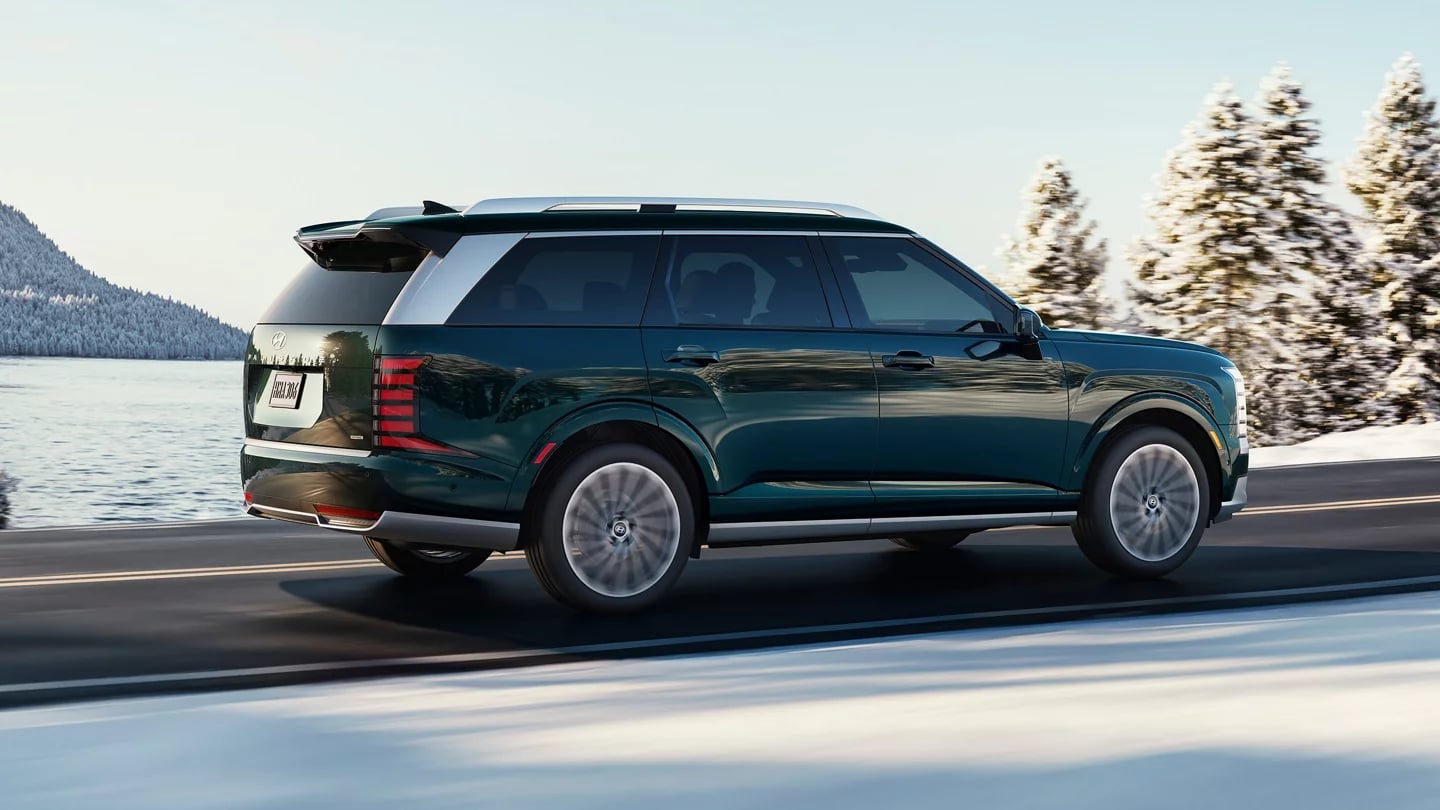 A dark green Hyundai SUV driving along a scenic snow-covered lakeside road.
