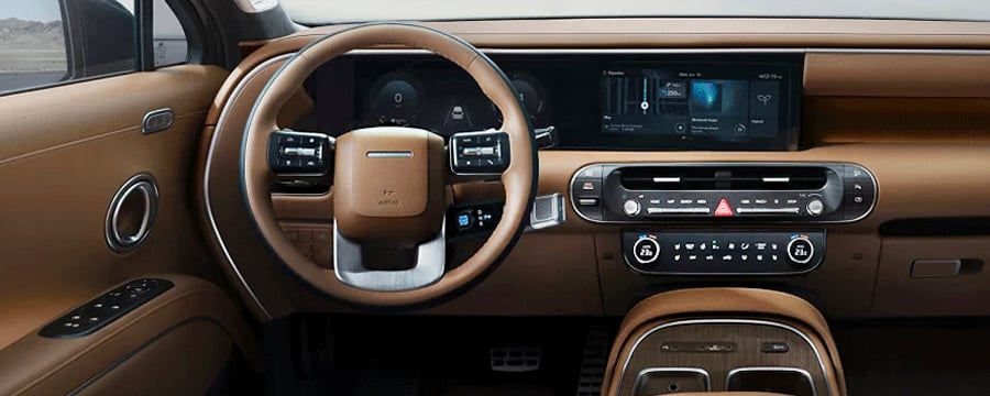 Tan leather dashboard and steering wheel of a modern car featuring dual digital display screens and climate controls.