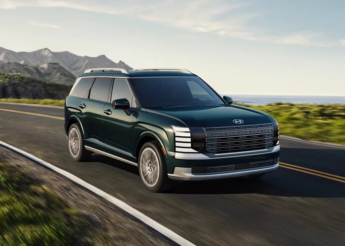 Dark green Hyundai SUV driving along a scenic coastal highway with mountains in the background.