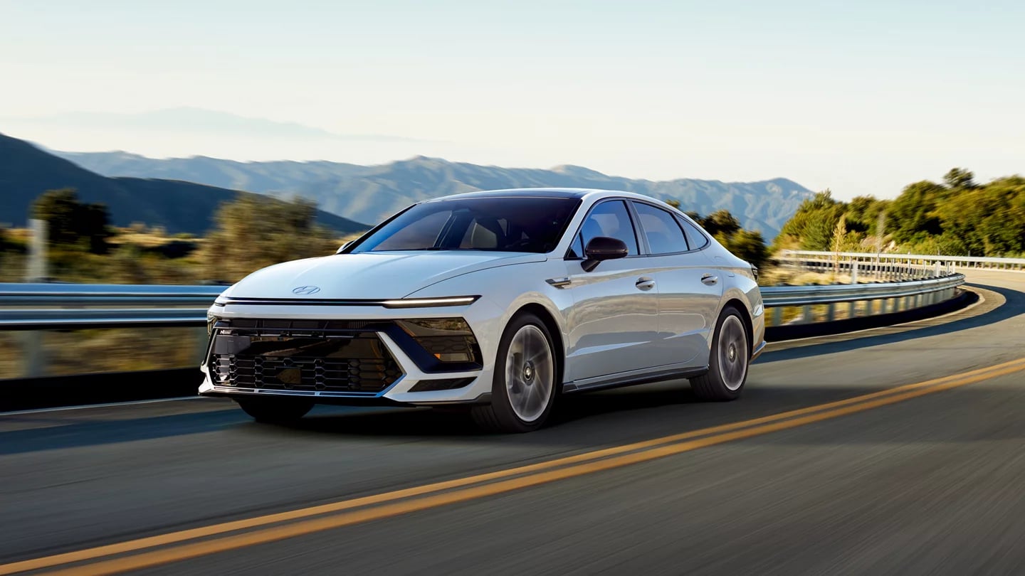White Hyundai Sonata sedan driving along a scenic mountain highway curve.