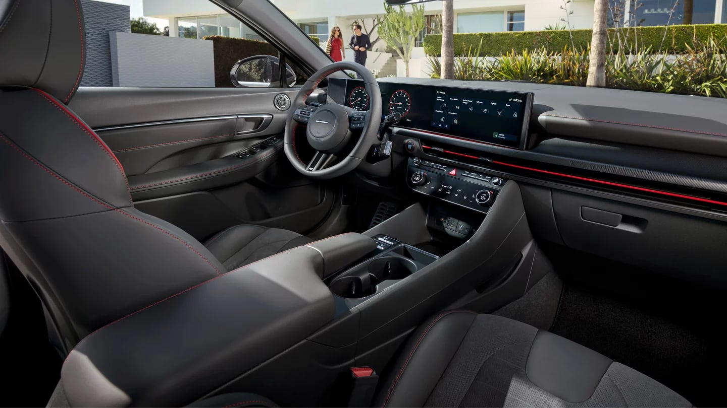 Interior view of a modern car featuring a digital dashboard, leather steering wheel, and red stitching.