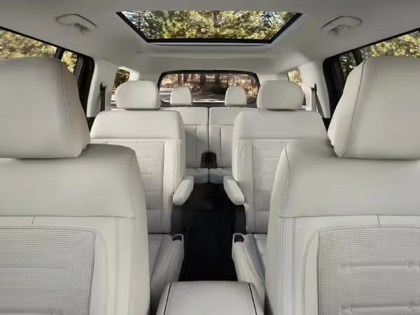 View looking back at second-row captain's chairs, third row, and panoramic sunroof in a white leather SUV interior.