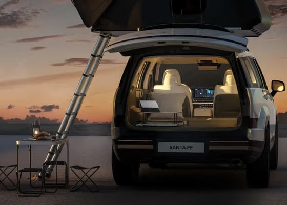 Rear view of a white Hyundai Santa Fe set up for camping with a rooftop tent and camping table at sunset.