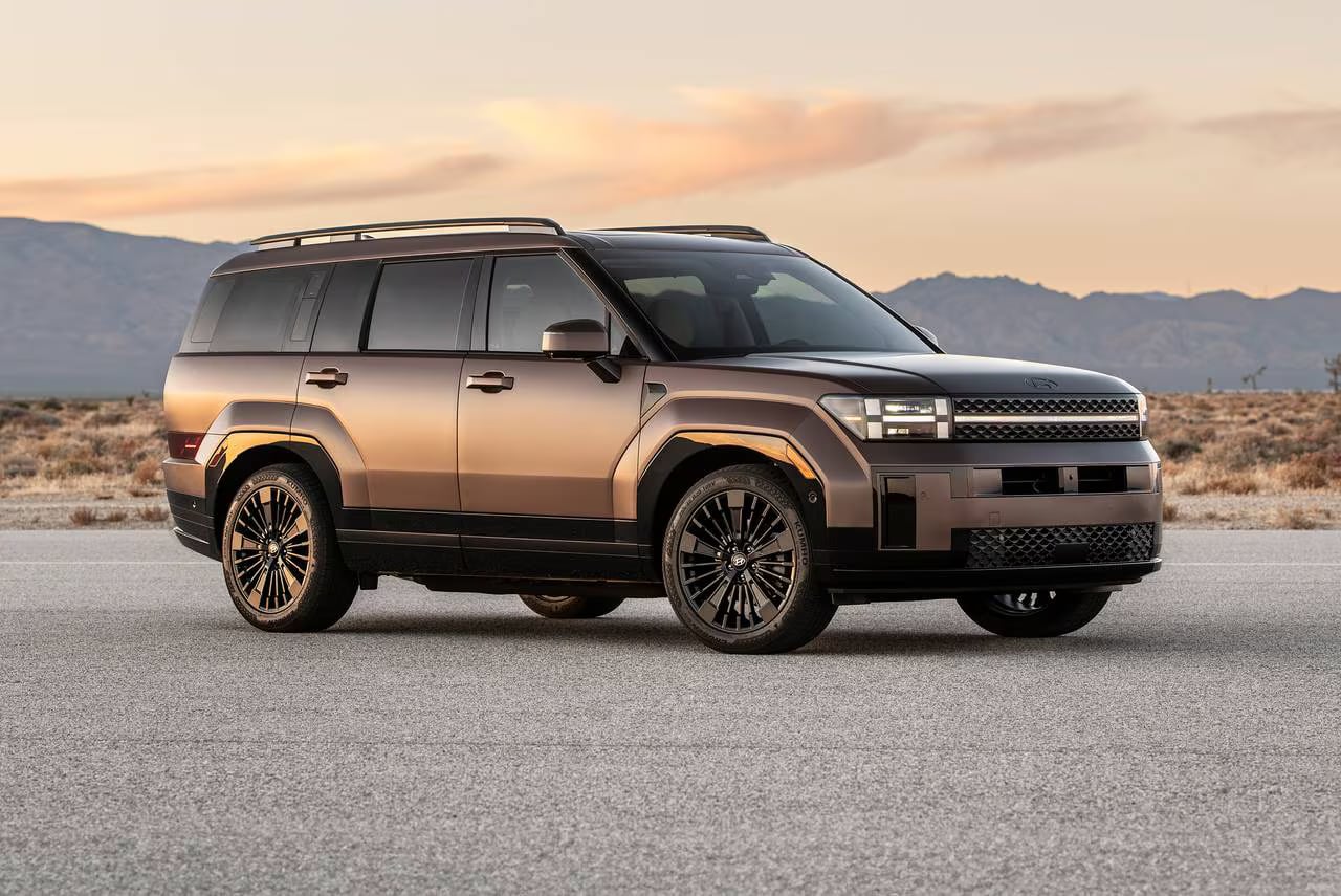 Bronze 2024 Hyundai Santa Fe SUV parked on an open road in a desert landscape at sunset.