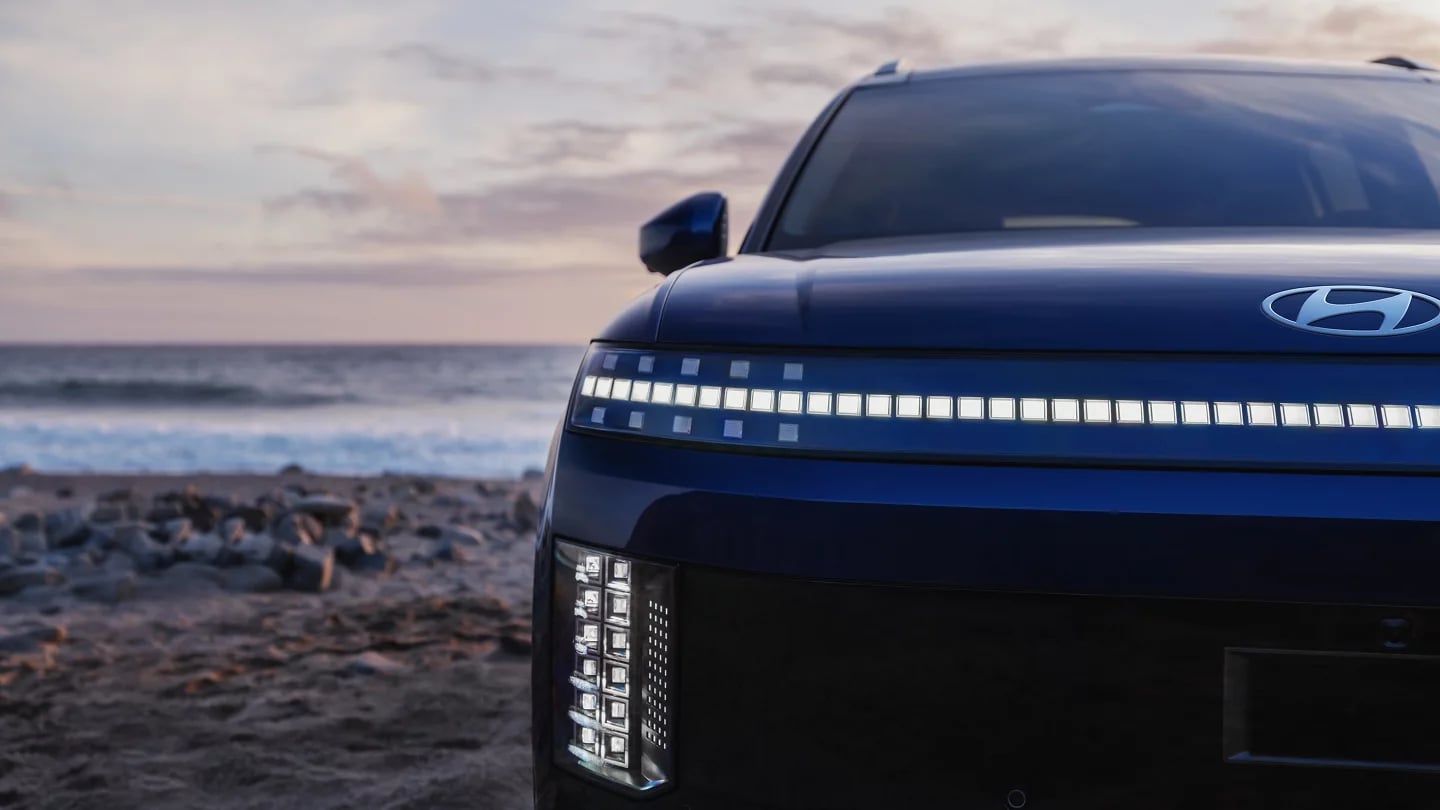 Front headlight and pixel LED light bar of a dark blue Hyundai vehicle parked on a beach at dusk.