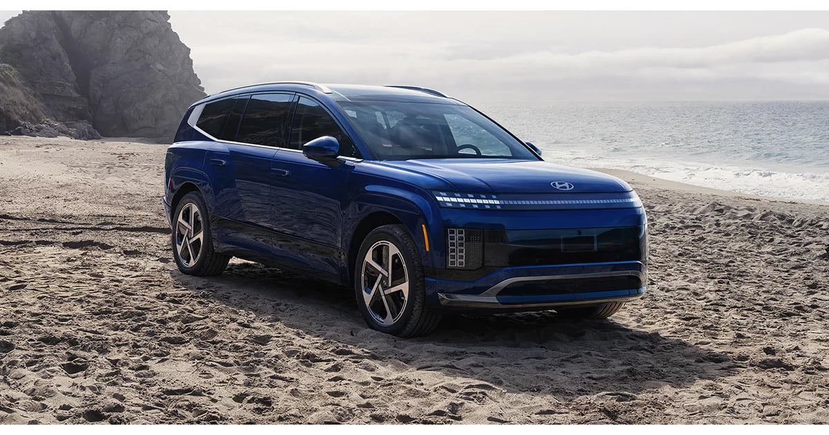 Metallic blue Hyundai IONIQ 9 electric SUV parked on a sandy beach near the ocean.