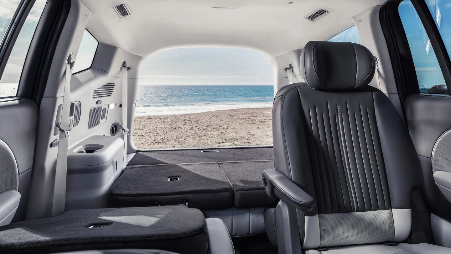 View from inside an SUV cargo area with folded seats, looking out the open tailgate onto a sandy ocean beach.