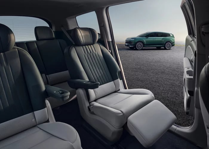 Spacious interior of a modern SUV featuring reclining captain's seats looking out at a green electric vehicle.