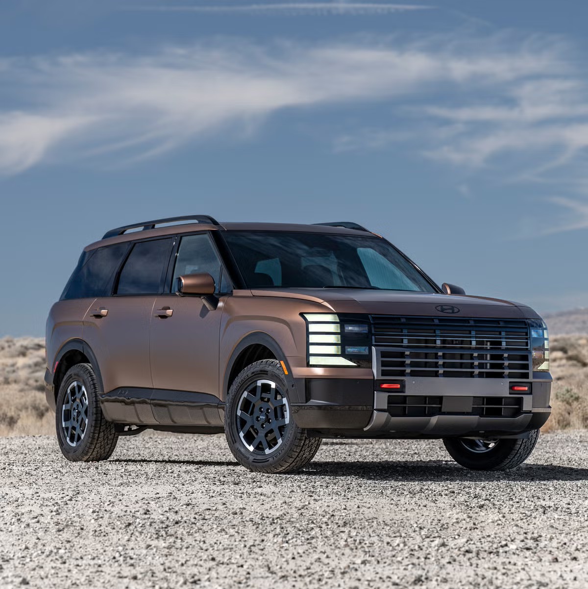 Brown Hyundai Palisade SUV parked on a gravel surface under a blue sky.