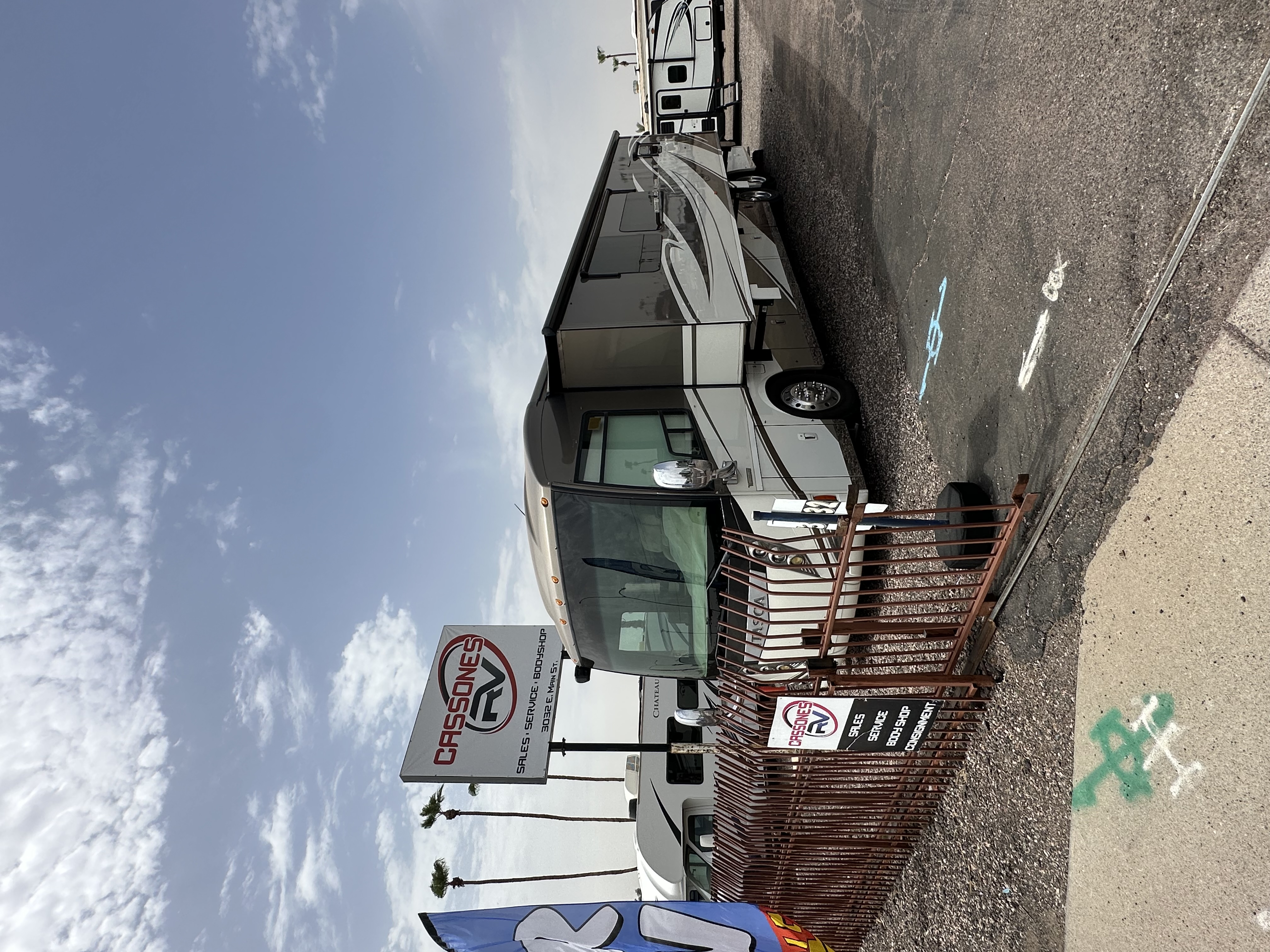 Class A motorhome parked behind a brown metal fence at Cassones RV dealership.