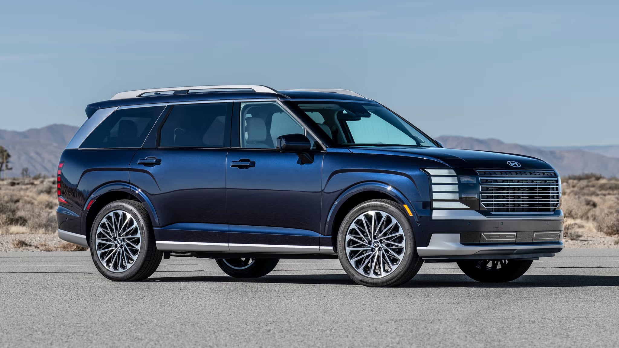 Side profile view of a dark blue Hyundai SUV parked on an open road in a desert environment.