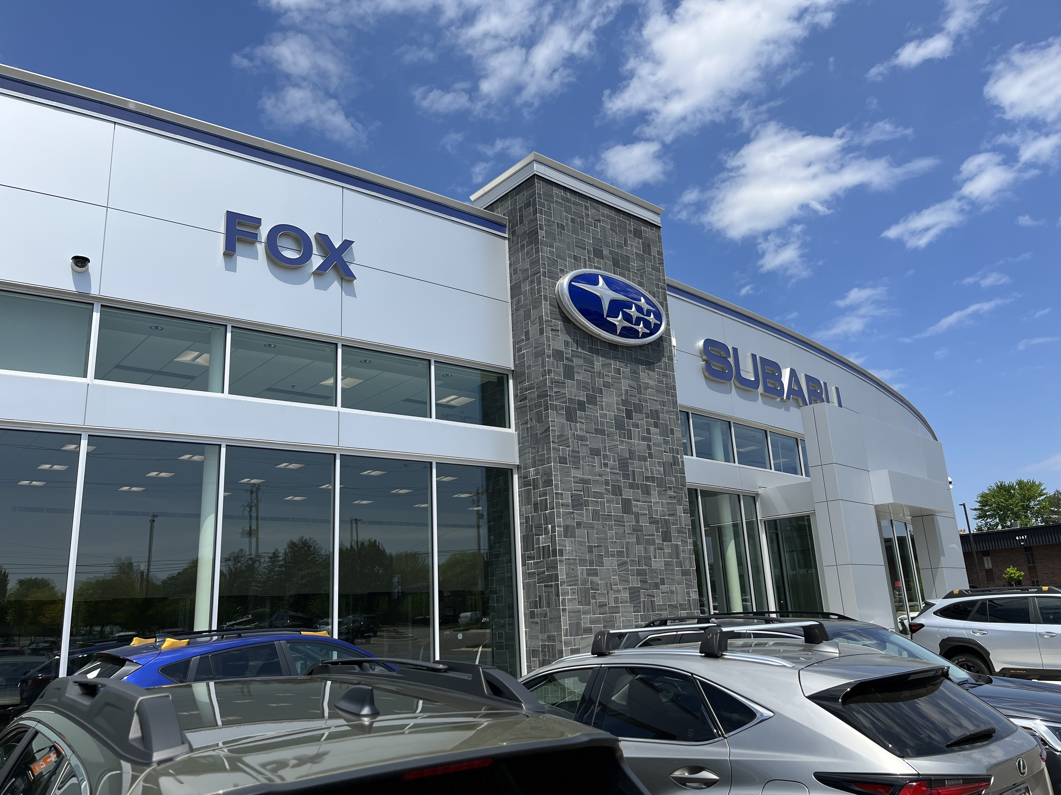 Exterior of Fox Subaru car dealership with modern glass and stone architecture under a blue sky.