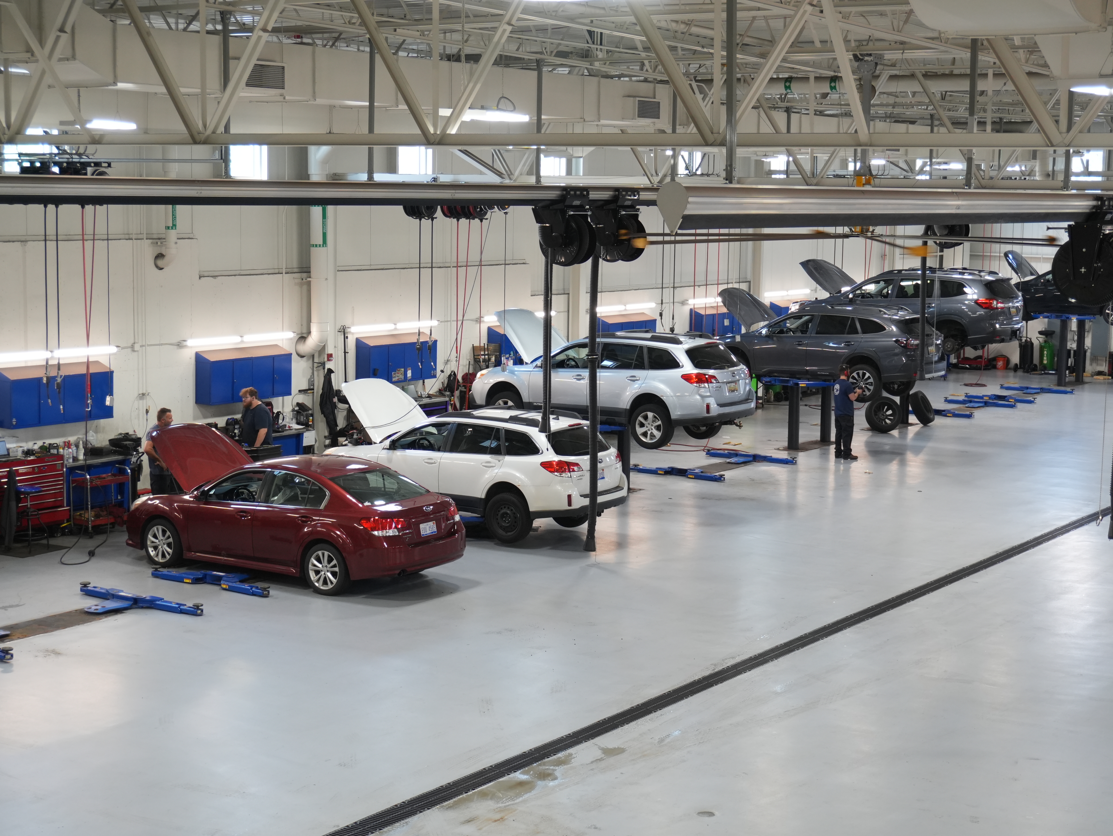 Several cars being serviced in a clean, professional automotive repair facility with mechanics working.