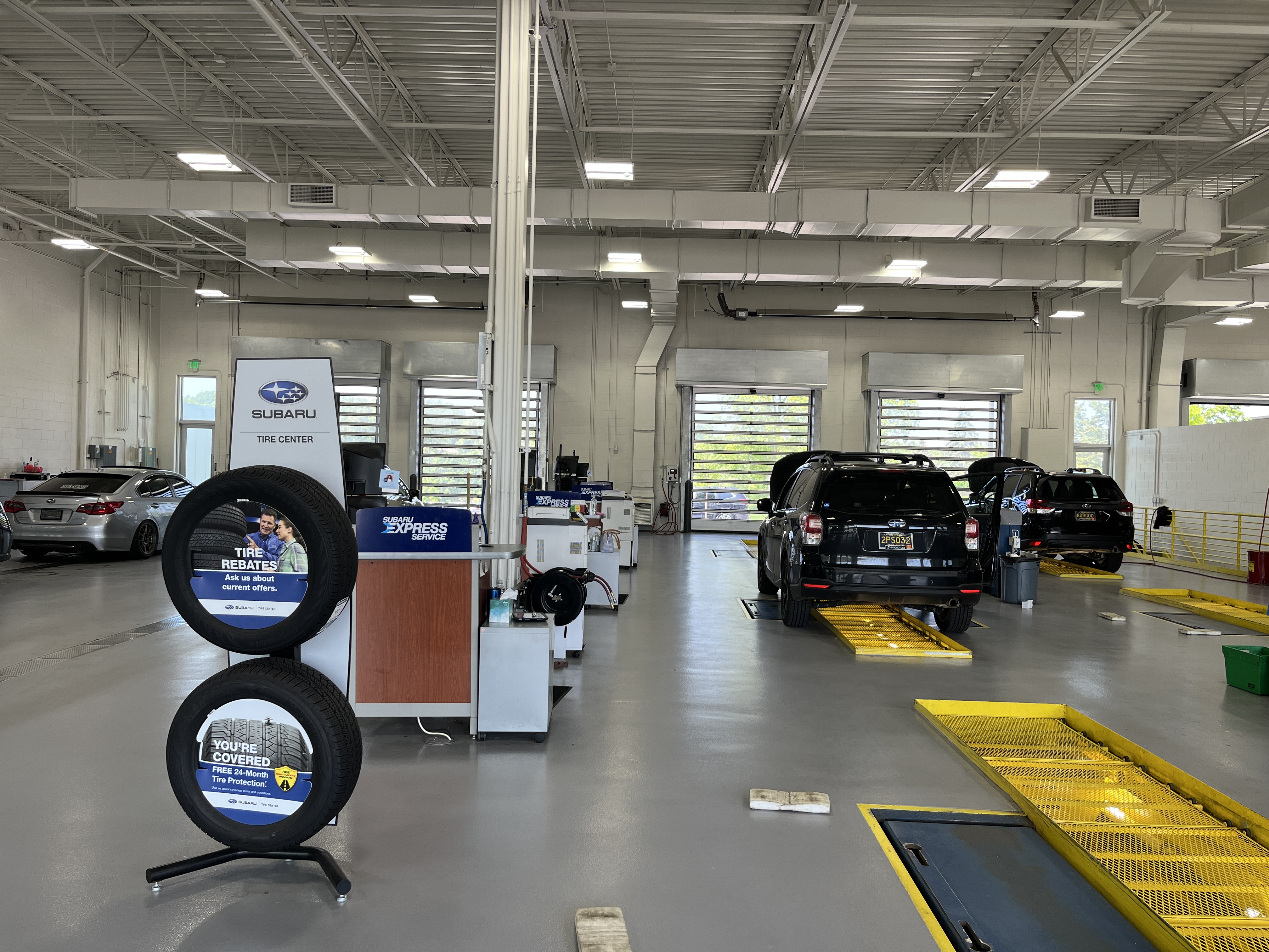 The clean, modern service bay of a Subaru tire center with cars on lifts and promotional tire displays.