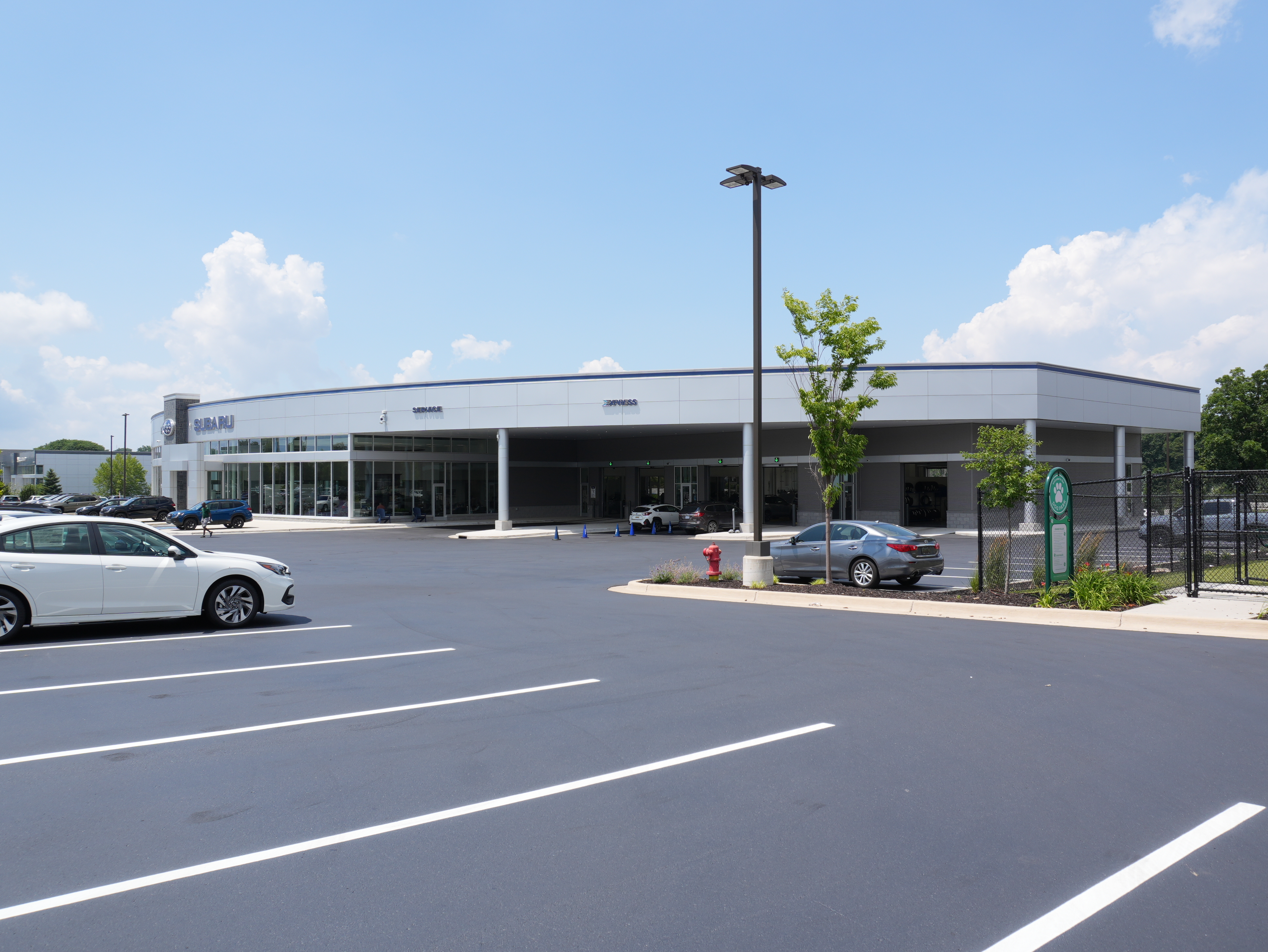 Modern Subaru dealership building with service bays and a large parking lot on a sunny day.