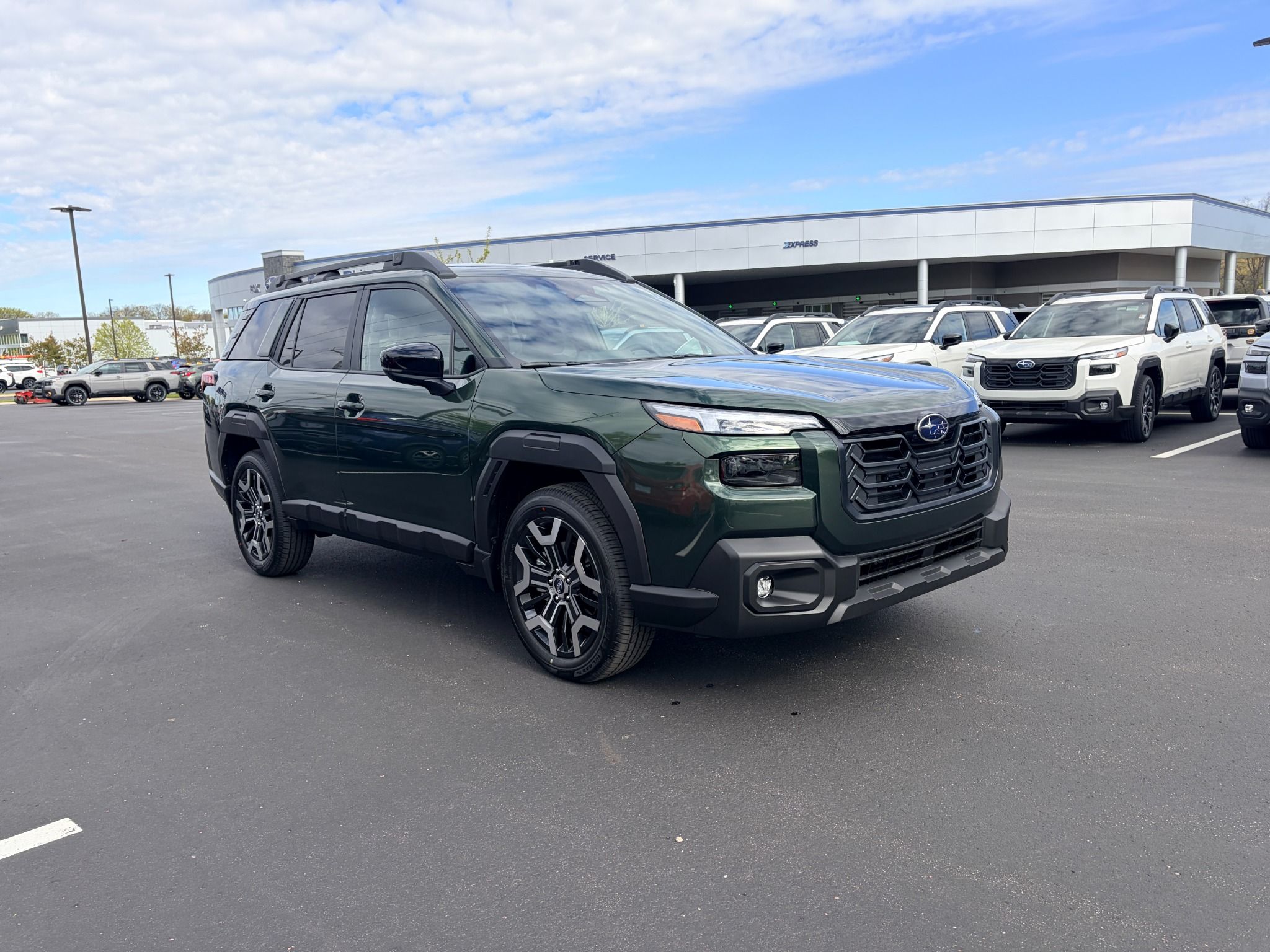 A dark green Subaru Forester SUV parked on a dealership lot on a partly cloudy day.