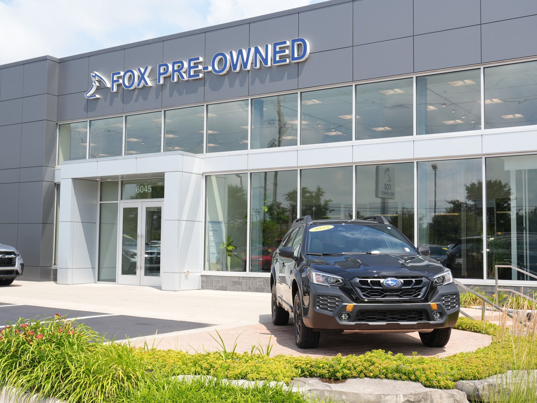 Black Subaru SUV parked in front of the modern Fox Pre-Owned car dealership building.