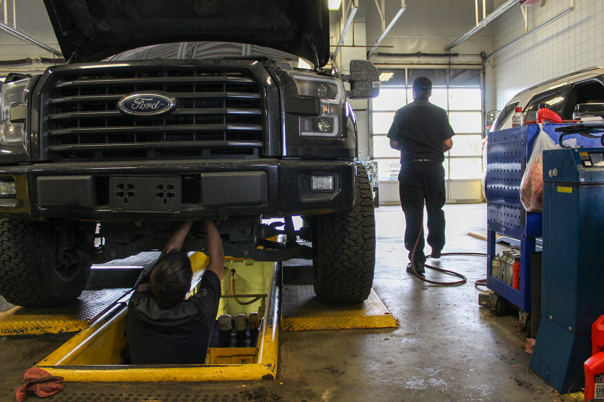 A mechanic working underneath a Ford truck in an auto shop service pit.