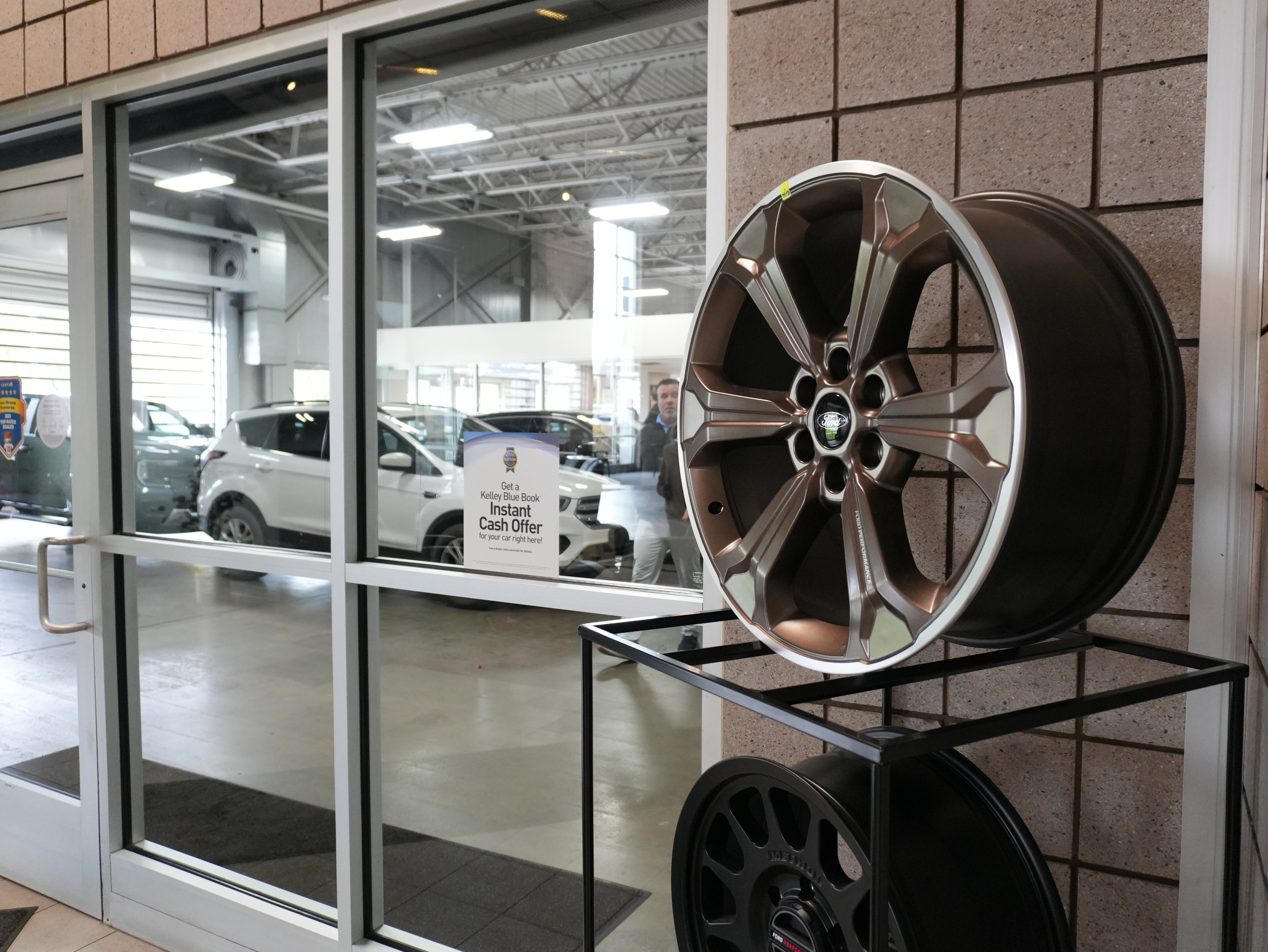 Bronze Ford Performance wheel on display at a dealership next to a glass door with cars inside.