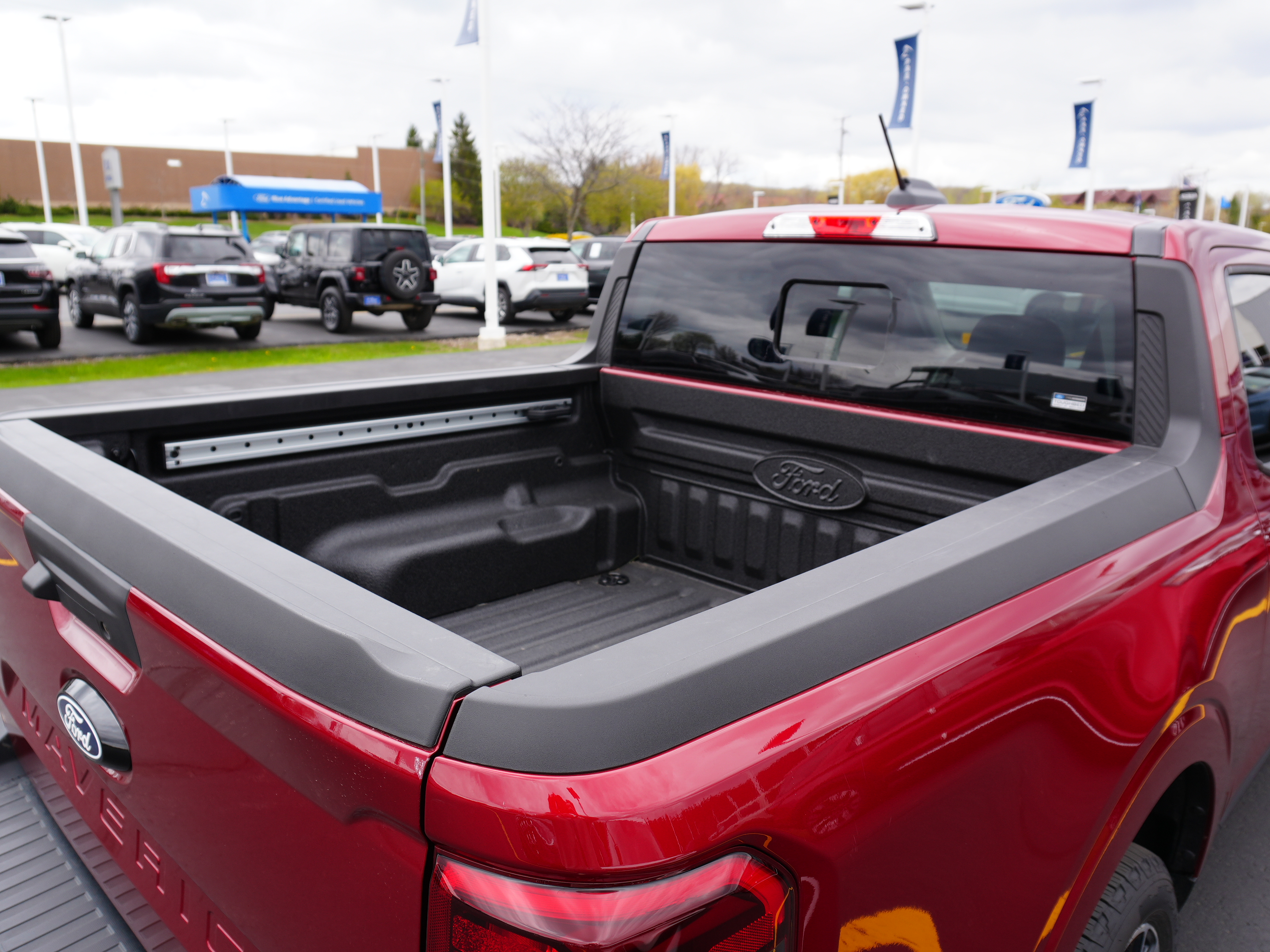 Red Ford Maverick pickup truck bed with a black spray-in bedliner and integrated Ford logo.