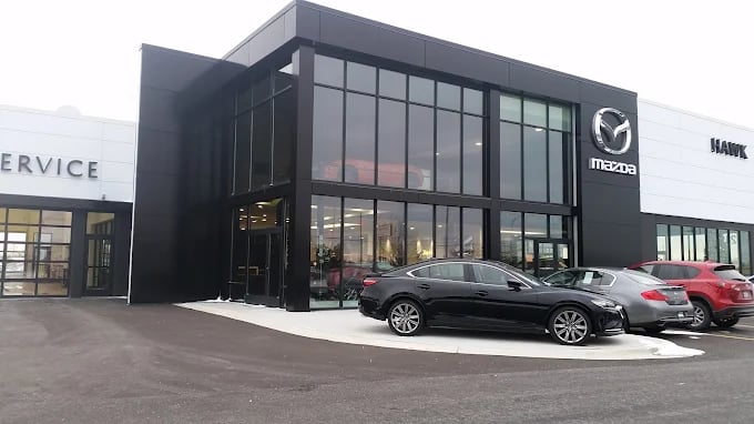 Exterior view of Hawk Mazda dealership featuring cars parked in front of a modern glass showroom.